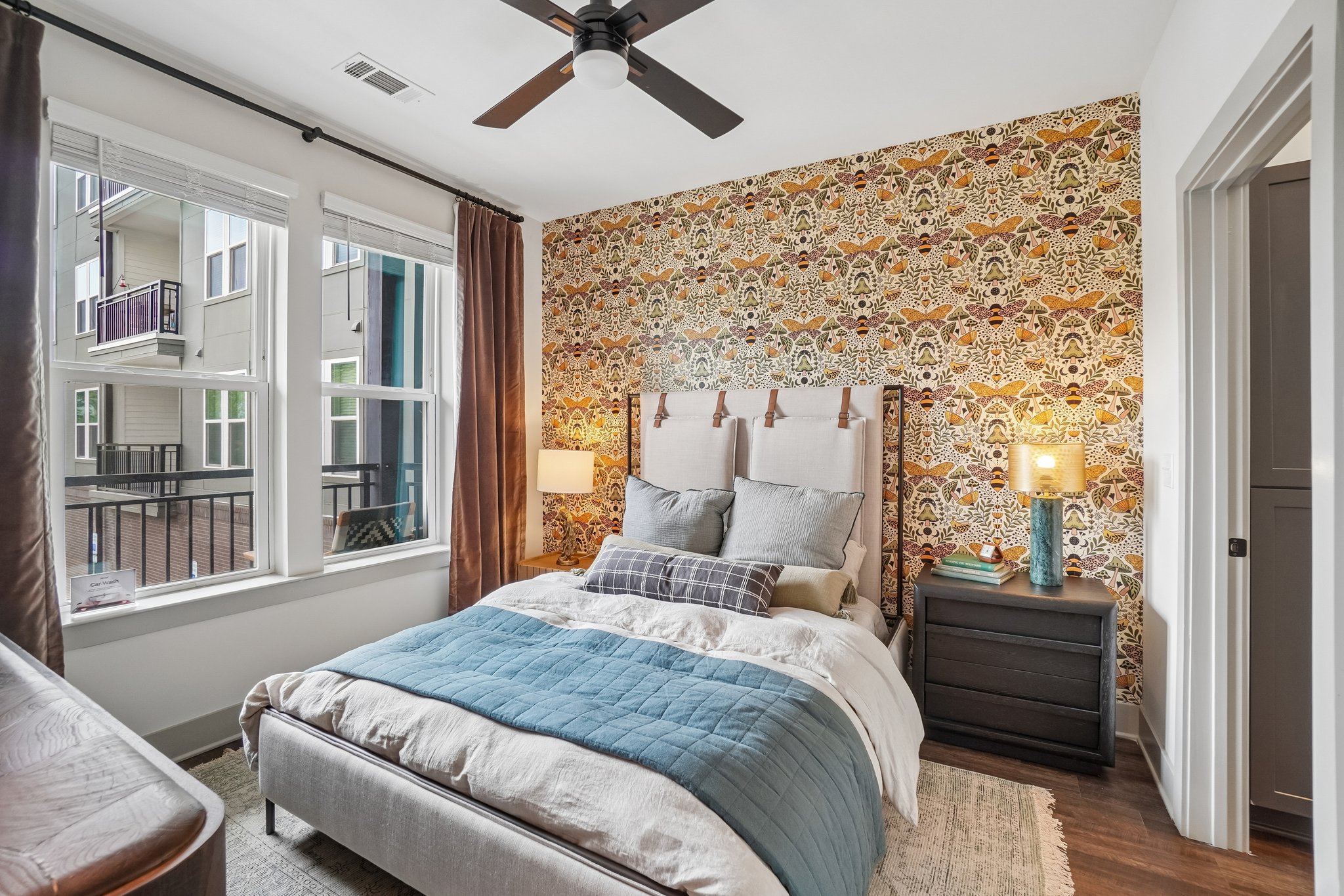 Model bedroom with accent wallpaper and ceiling fan at The Avery